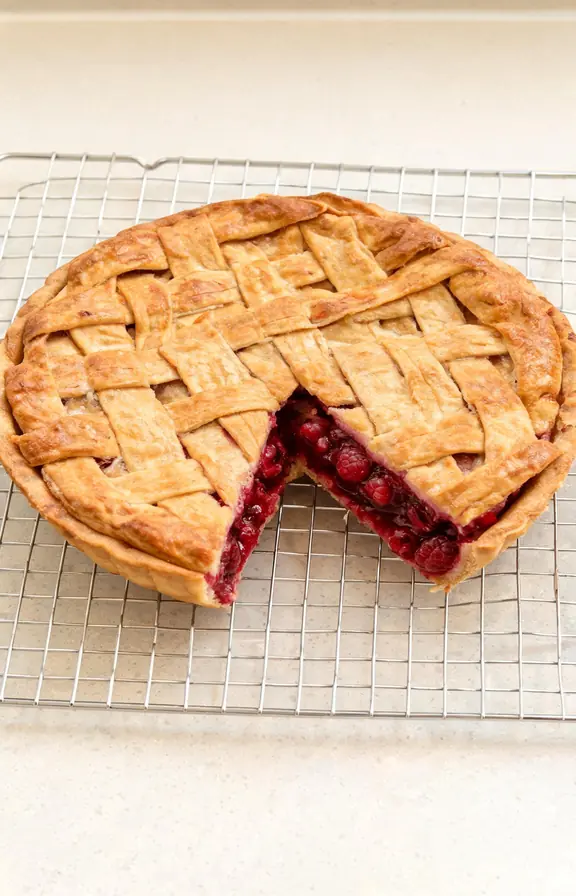 Whole raspberry pie with a golden lattice crust cooling on a wire rack