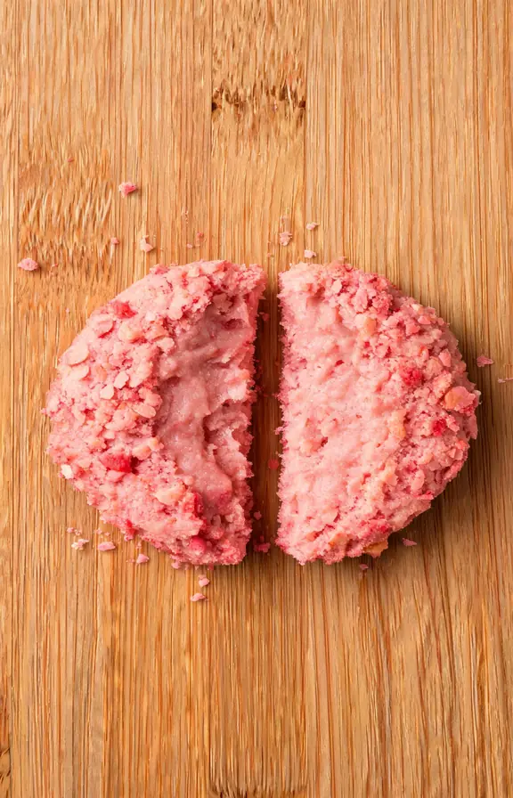 Close-up of a single strawberry crunch cookie broken in half showing a soft chewy pink interior